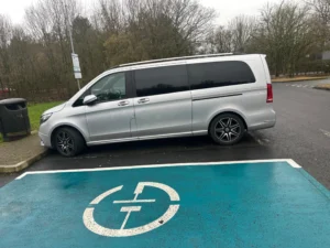 Silver Mercedes-Benz MPV parked near electric vehicle charging bay in a London car park on a cloudy day
